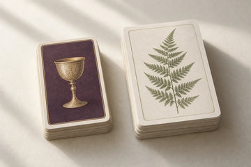 A plum tarot deck with a golden cup card beside a larger fern-patterned oracle deck
